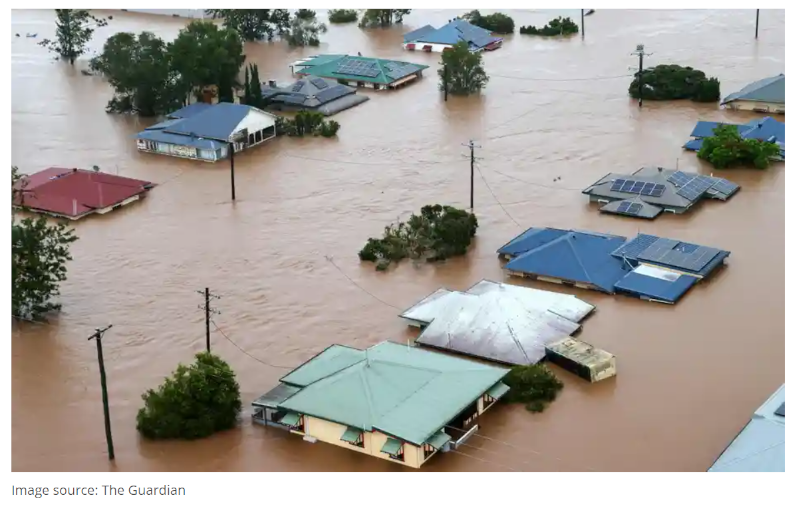 Aerial view of severe flooding with rooftops and solar panels partially submerged in muddy water.