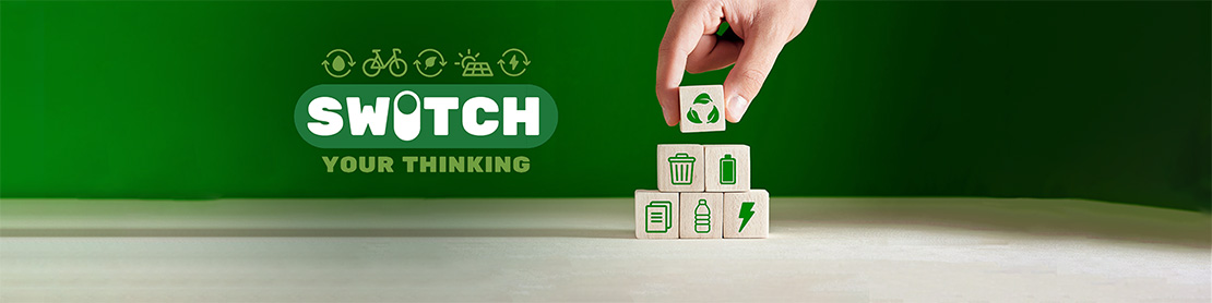 Hand placing wooden blocks with recycling icons under the slogan 'Switch Your Thinking' on a green background